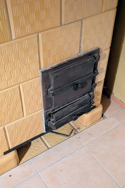 Ein goldener Kachelofen wird angeheizt. Die schwarze eiserne Ofenklappe ist noch geöffnet.