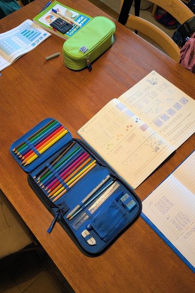 Auf einem Küchentisch liegen Arbeitshefte von Vorschul- bzw. Grundschulkindern. Das Vorschulheft beschäftigt sich mit Zahlen, Mengen und Formen. Das zweite Heft ist ein Matheheft der zweiten Klasse mit Rechen- sowie Sachaufgaben.
