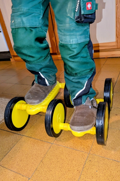 Ein Junge in grüner Hose fährt in einer Küche auf einem gelben Kunststoff-Pedalo.