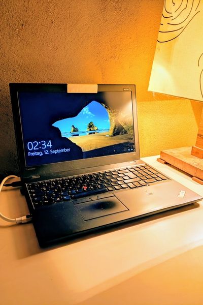 Ein Laptop steht auf einem Tisch- Die Tischleuchte ist nur halb zu sehen. Die Uhr zeigt 2:34 Uhr morgens an.