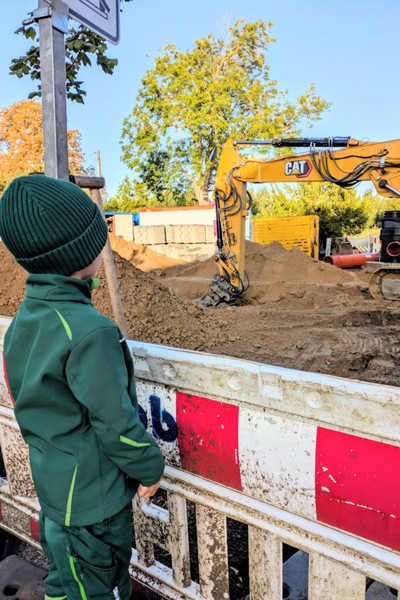 Ein Junge steht vor einer Baustelle mit einem Bagger.
