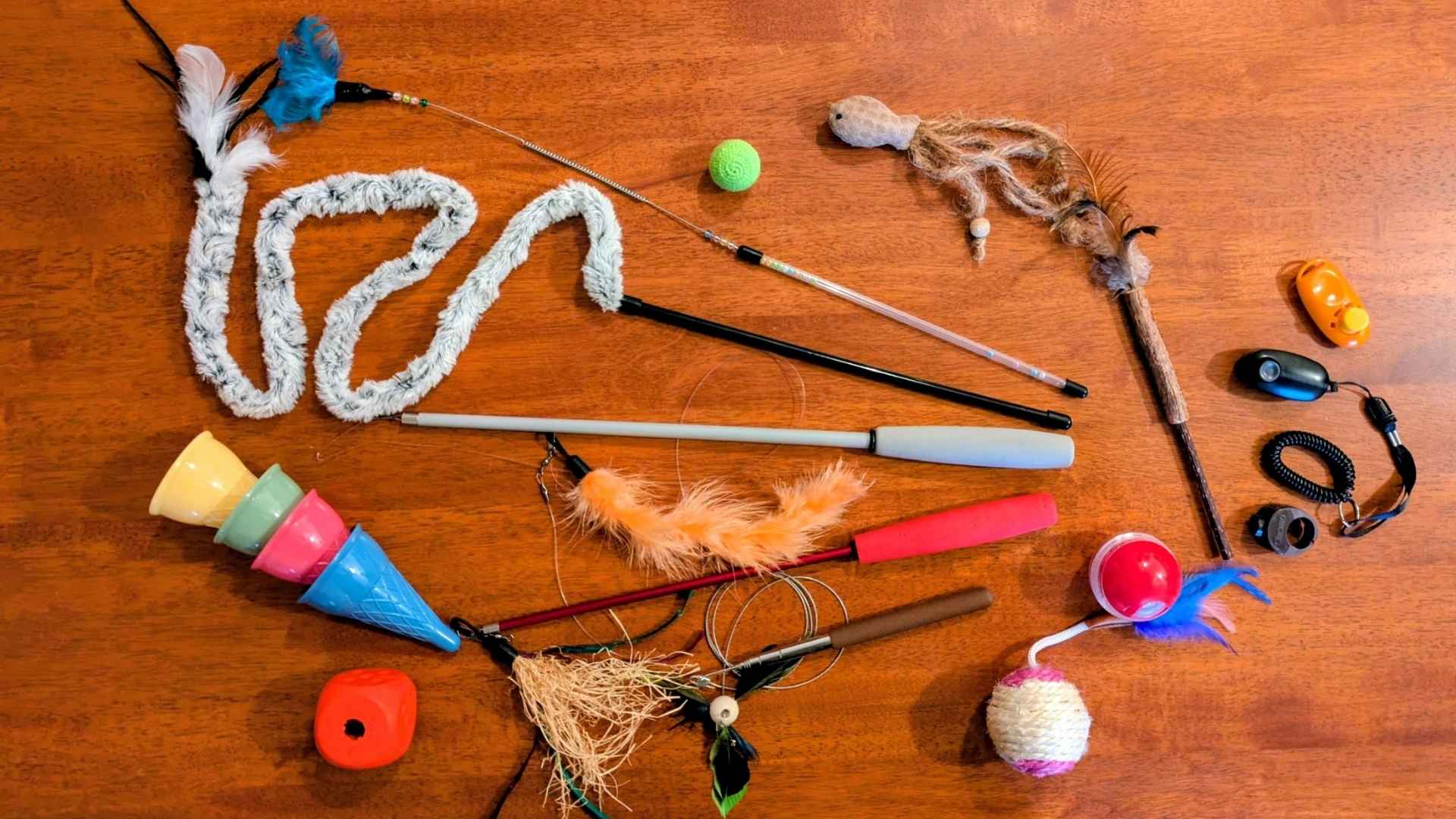 12-von12-dezembder-2025-beitragsbild-spielzeug Verschiedenes Spielzeug für Katzen liegt auf einem Küchentisch: Angeln, Bälle, Snackbälle, Clicker, Federwedel usw.