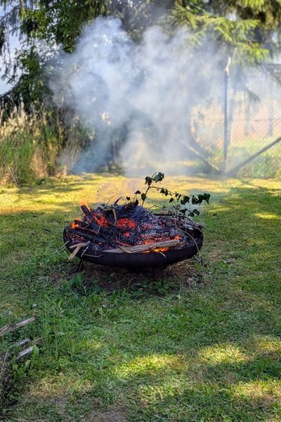 Im Garten brennt ein kleines Feuer in einer großen Feuerschale. Etwas Rauch steigt auf.