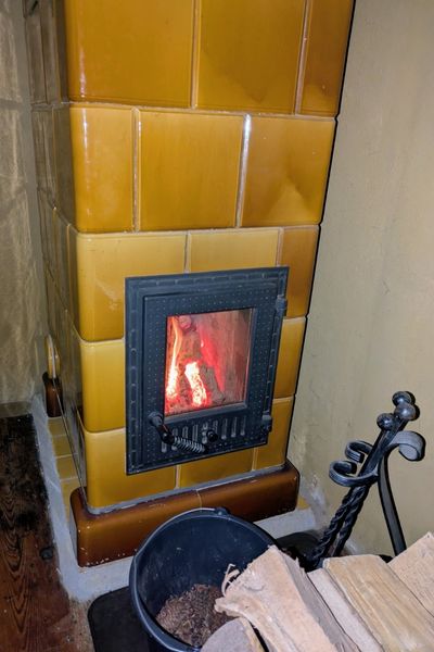 Ein goldener Kachelofen ist mit Holz bestückt. Das Feuer brennt gut.