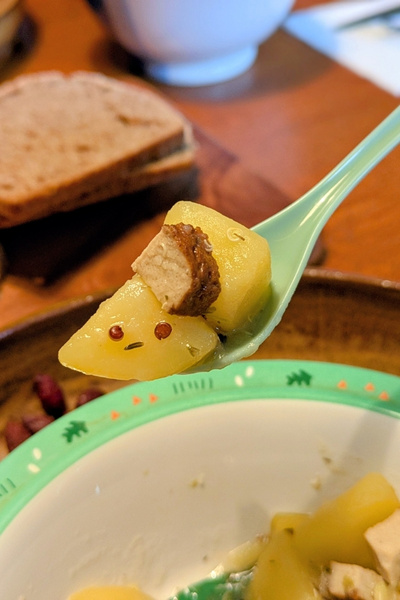 Kartoffelstückchen auf einem Löffel übe reiner Suppenschüssel. Auf dem Kartoffelstück ist ein Gesicht aus Kräutern entstanden.