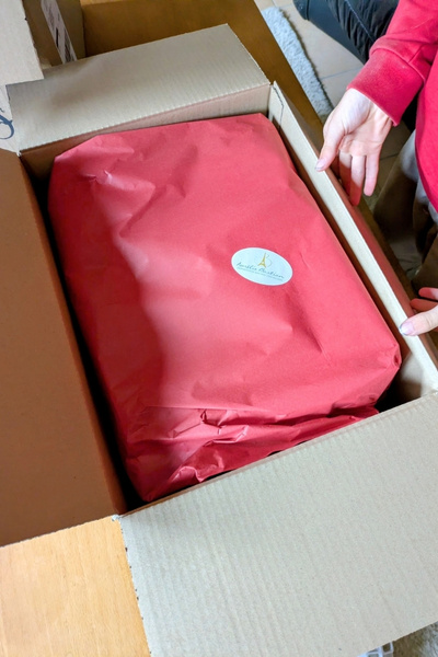 Ein Junge öffnet einen Karton. Darin liegen in rotem Seidenpapier hübsch verpackt Backformen.