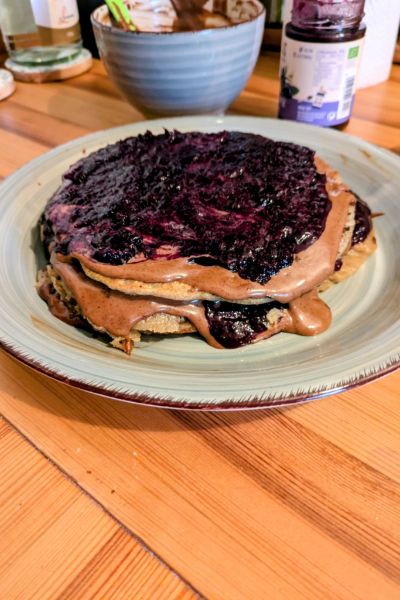 Derselbe Pfannkuchen ist aufgeschichtet mit zwei weiteren Pfannkuchen, Heidelbeermarmelade und Carobcreme.