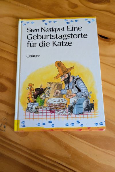Auf einem Holztisch liegt das Buch "Eine Geburtstagstorte für die Katze" von Sven Nordqvist.