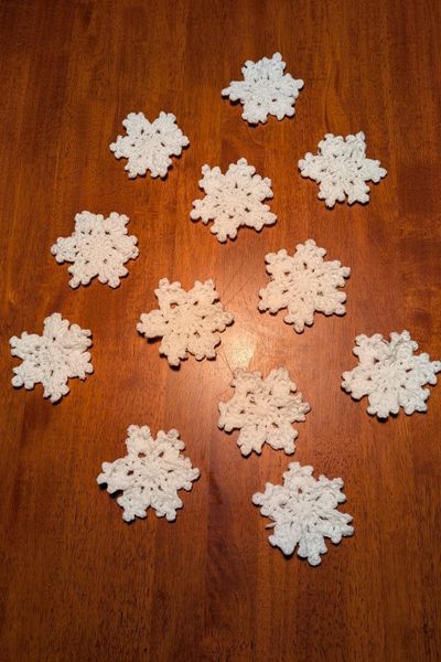 12 Häkelsterne aus weiß glitzernder Polyesterwolle liegen zum Plätten auf einem Küchentisch.