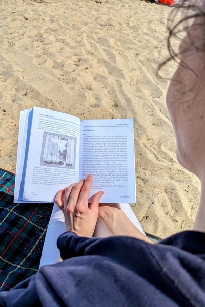 Ausschnitt einer Katzenberaterin, die am Strand sitzt und ein Buch über Katzen liest.