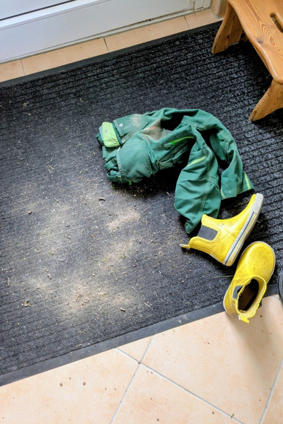 Eine Kinderhose liegt auf einer Schmutzfangmatte, daneben ein paar Kinderschuhe und ein kleiner Berg Sand.