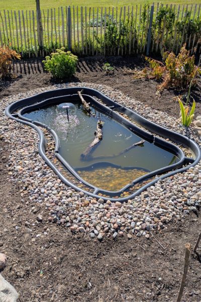 Ein Gartenteich wird angelegt und ist mit Kiessteinen und ersten Blumen umrandet.