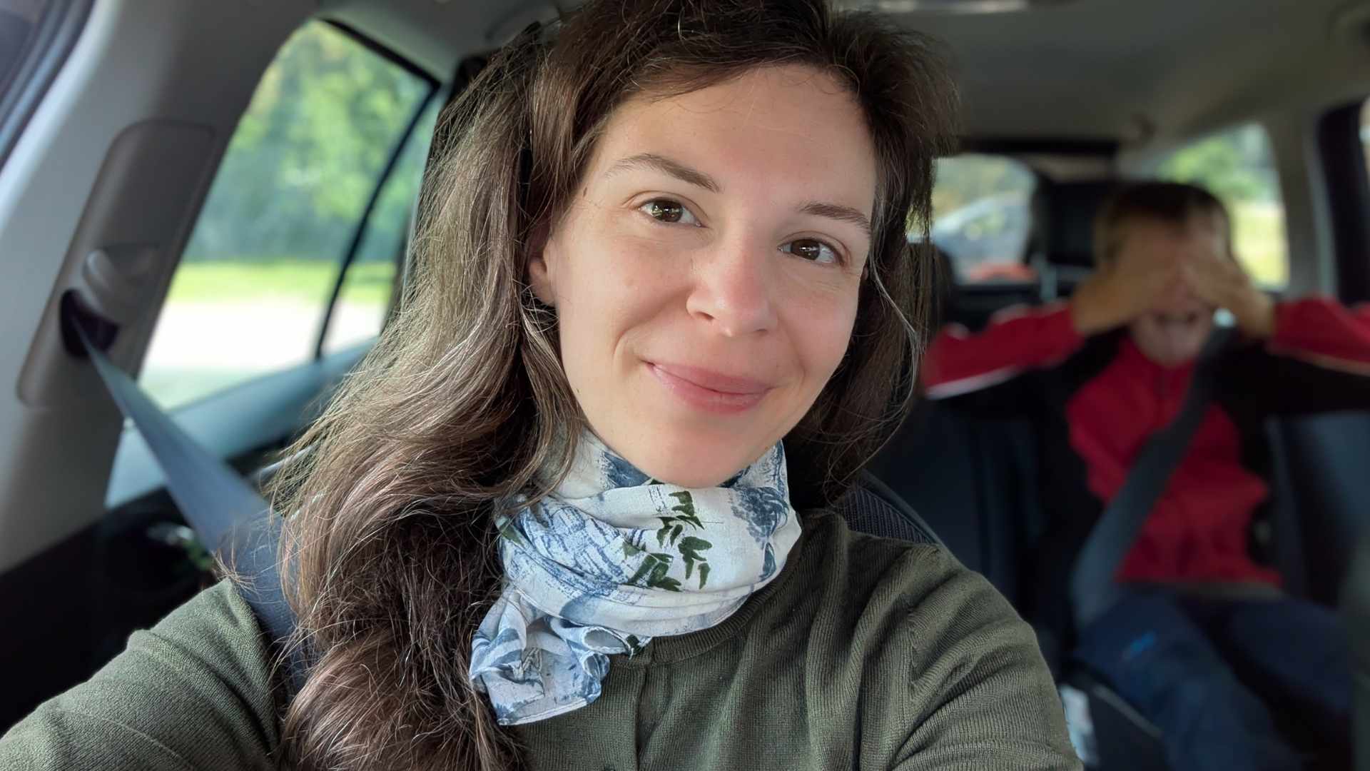 Dies ist ein Selfie im Querformat. Es zeigt eine Frau im Auto auf dem Beifahrersitz. Die Frau hat den Kopf etwas seitlich gelegt und schaut müde und glücklich in die Kamera.